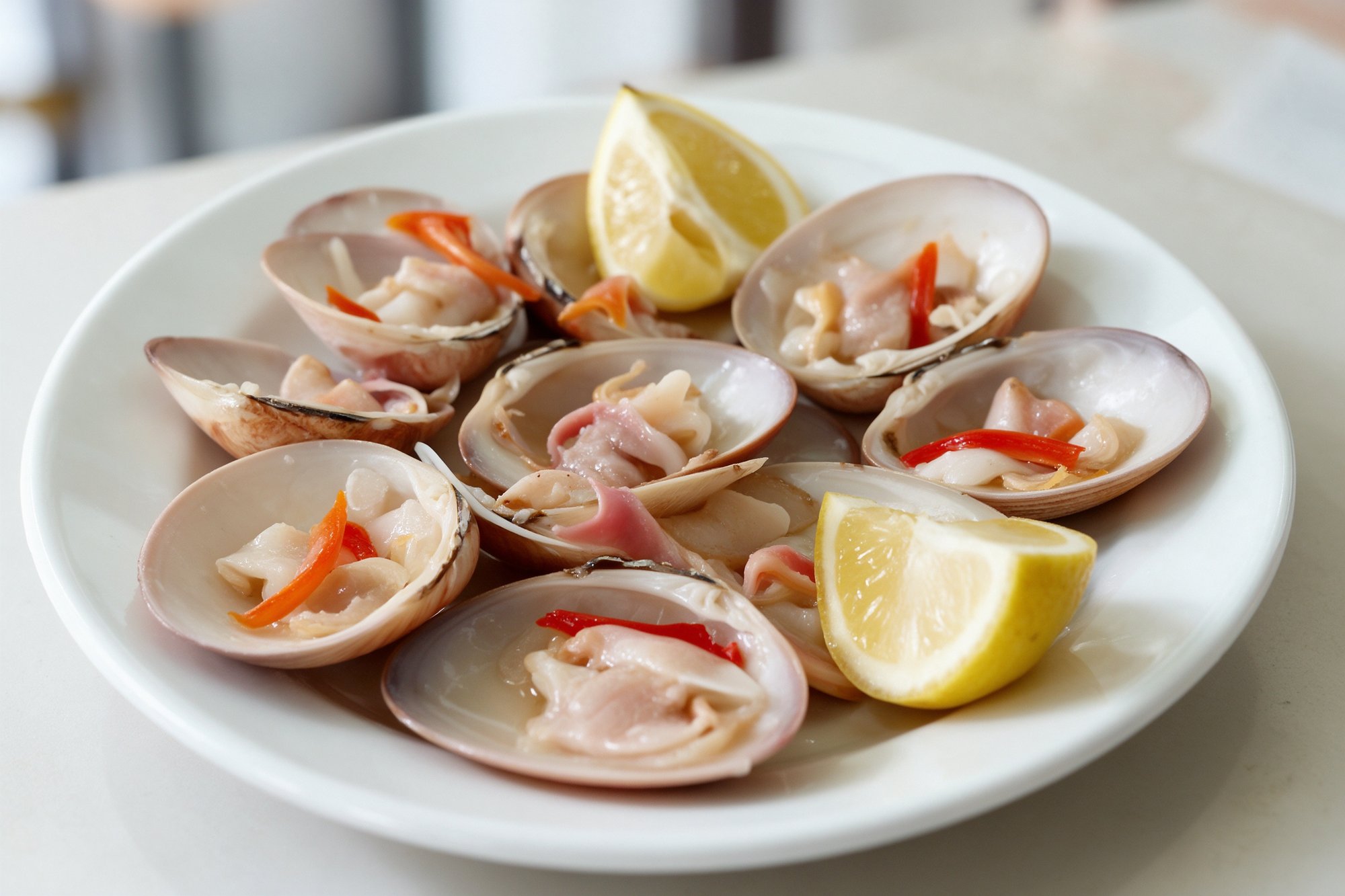 Almejas frescas abiertas en su concha con tiras de pimiento asado y gajos de limón en plato blanco